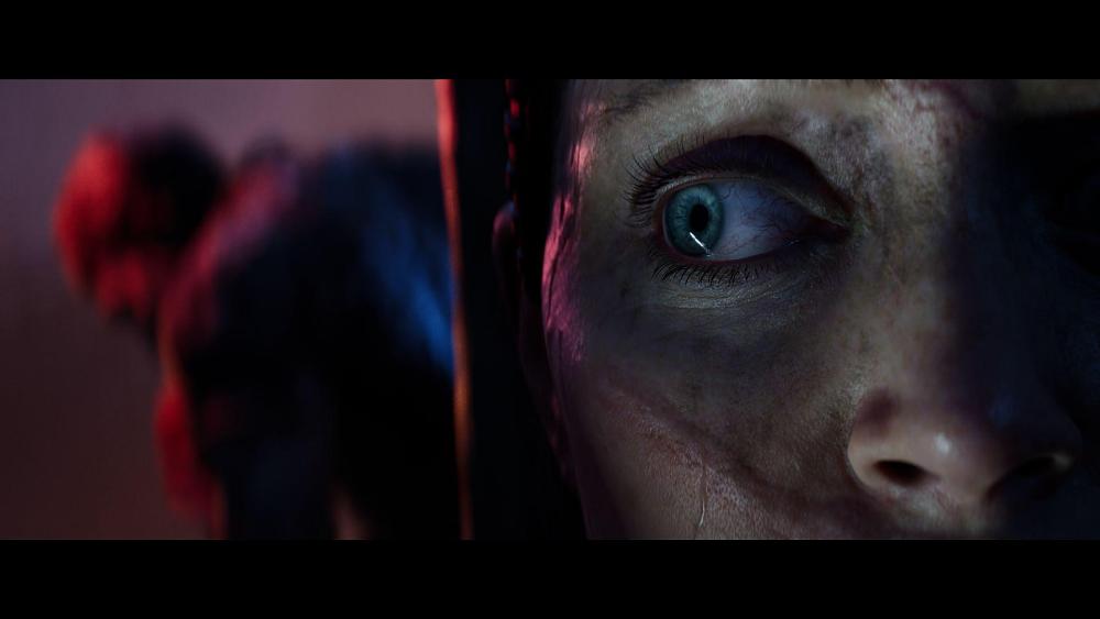 An intense close-up of Senua from Hellblade 2 as a figure lurks in the background.