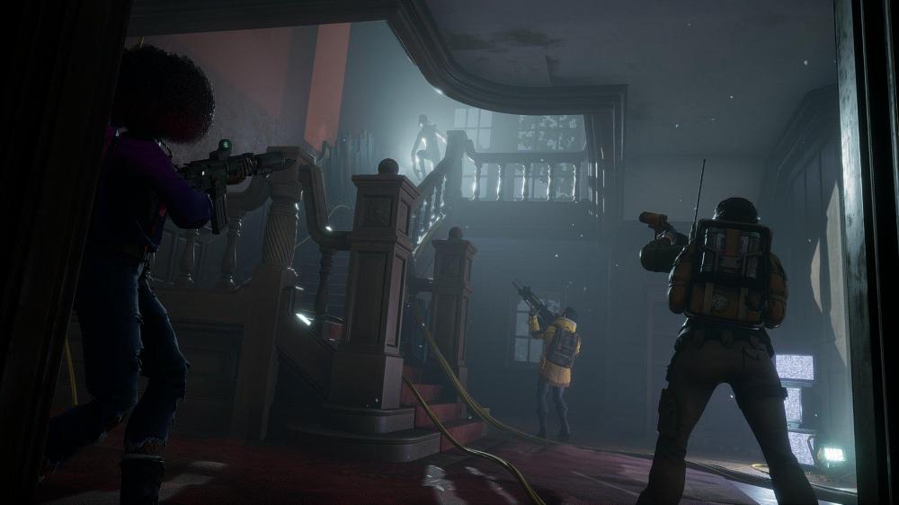 Image from Redfall set in a lived-in mansion that’s fallen into disrepair with a backlit vampire at the top of a wooden staircase with three heroes with their weapons at the ready staring up from the base of the stairs.