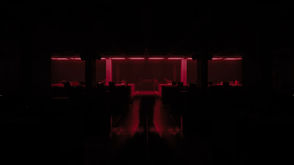 A dark office. A line of dim red lights in the far back are turned on. Beneath them are humanoid figures standing at awkward angles.
