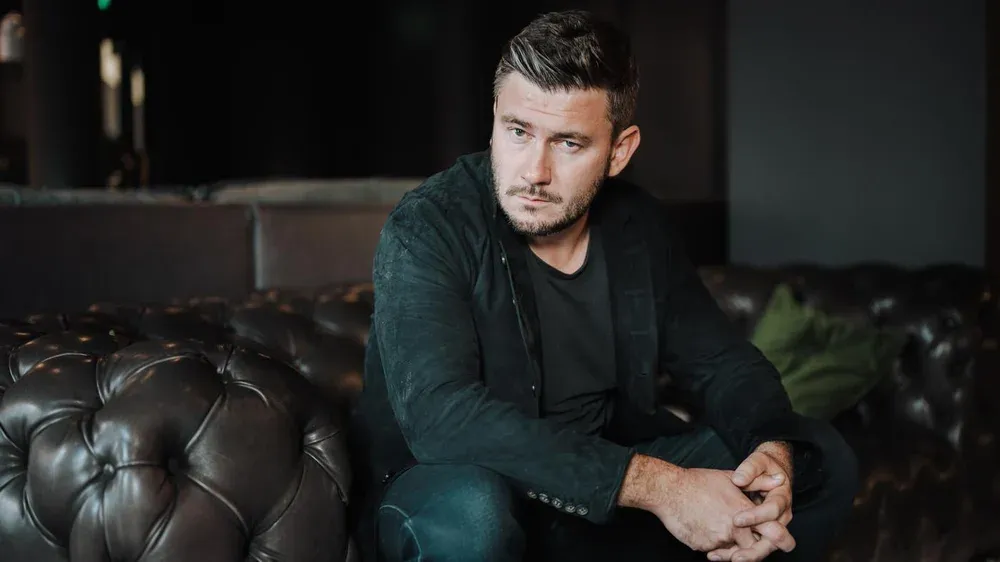 Photograph of a Russian author, Dmitry Glukhovsky, sitting on a leather couch.