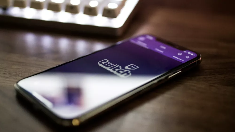 Photo of the Twitch logo on a phone sitting on a desk by Caspar Camille Rubin on Unsplash.
