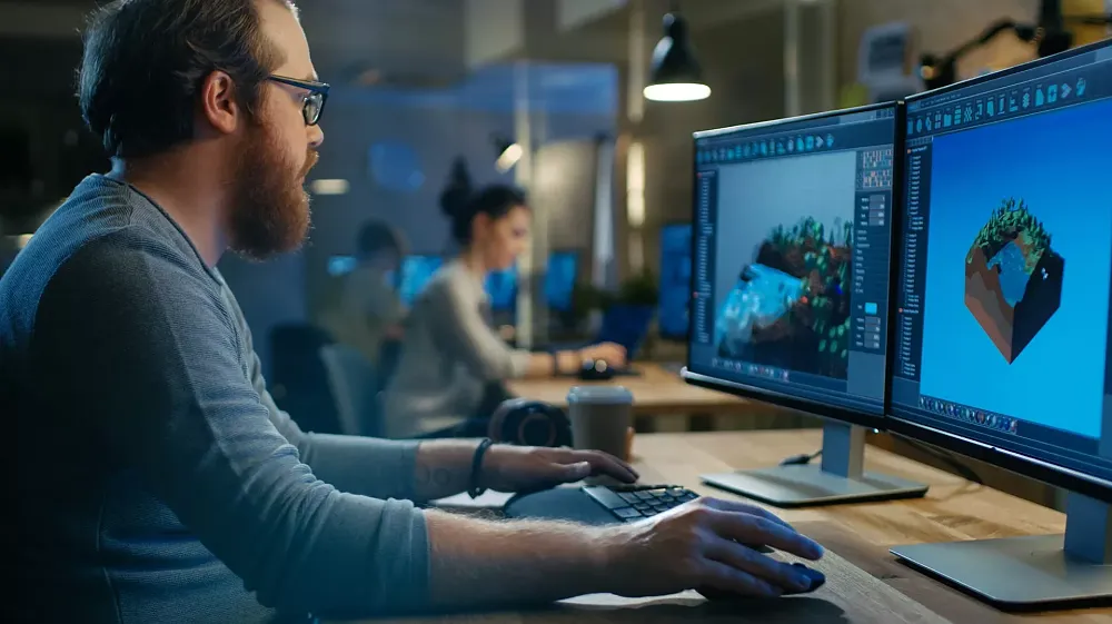 A bearded man sitting at a desk and working on developing a new video game.