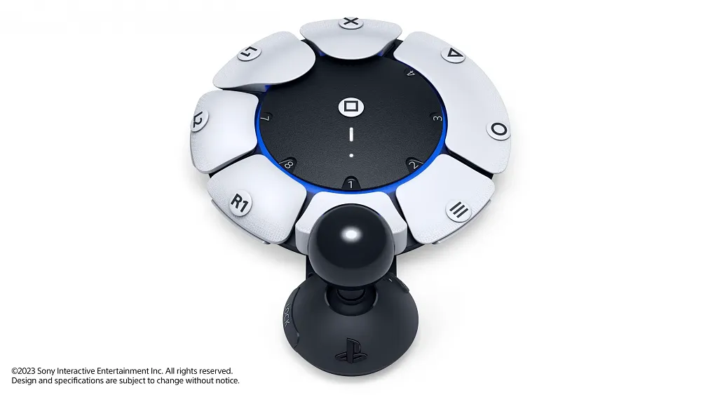 Photo of a round almost flat PlayStation 5 controller with several accessibility options. The outside edge of the controller feature large, easy to press white buttons. The middle is black and looks like another big button. The bottom has a large joystick attached to the controller. Each button has a symbol on it like those found on typical PlayStation 5 DualSense controllers.