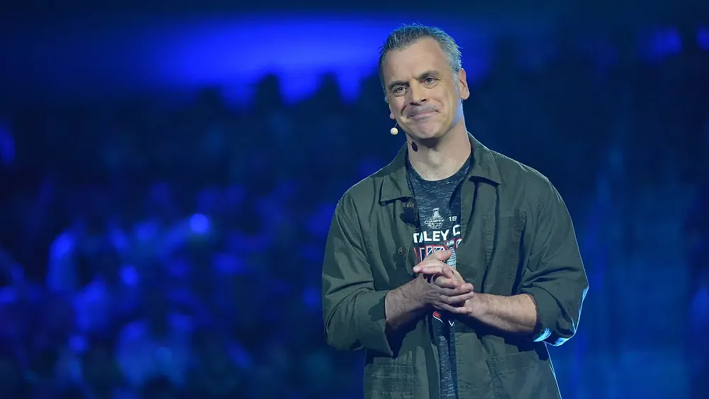 A photograph of a man, Pete Hines, clasping his hands together and smiling.