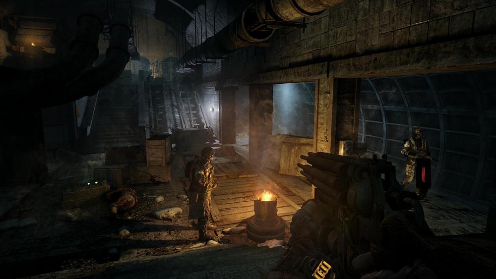 Your character hiding in the shadows with a weapon in hand. In front of them is a person standing near a fire-filled barrel. Another person is walking down a side pathway. The entire scene looks to be in an old metro station that has been converted into a place to live.