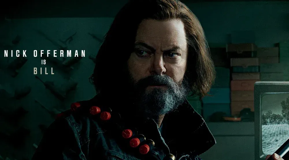 A man with long hair and a long, greying beard holding a weapon. There is are shotgun shells on a bandolier over his right shoulder. On the left it says "Nick Offerman is Bill."