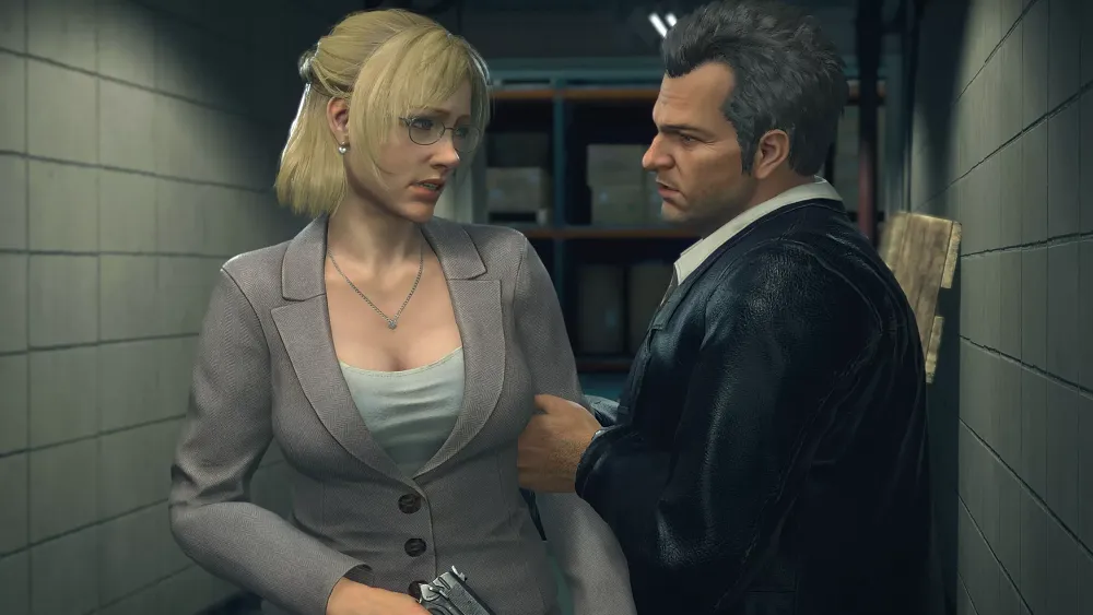 A woman with short blonde hair in a grey business suit standing next to a man with slicked back hair wearing a black leather jacket.