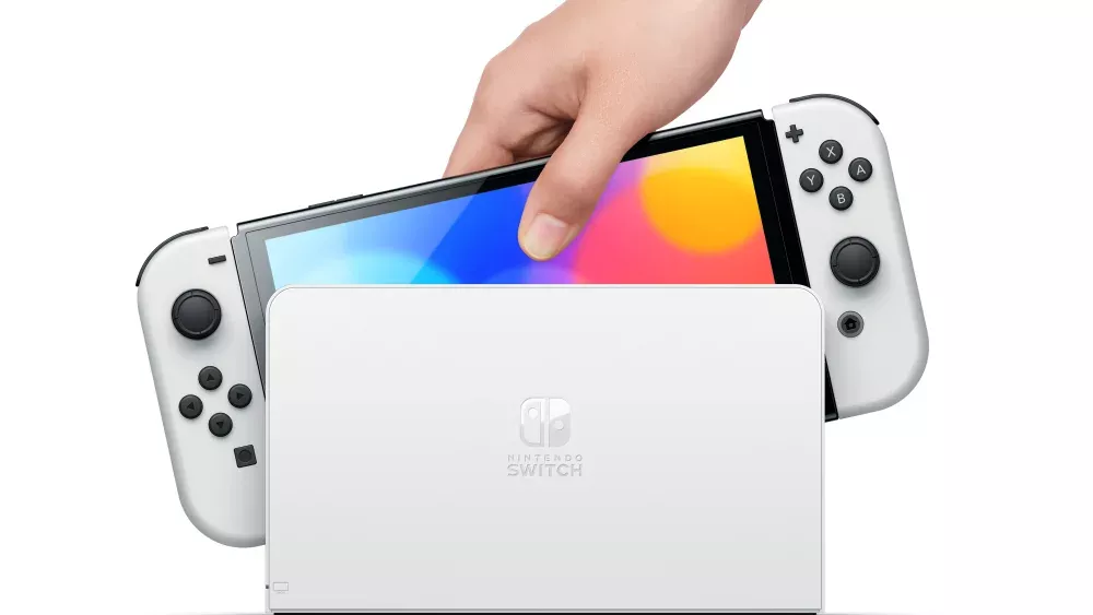 A person's hand picking up a Nintendo Switch OLED from a Switch Dock.