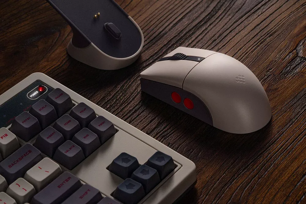 A photo of a mouse that uses the same color scheme of the original NES controllers. It's sitting on a desk next to other retro styled peripherals and items.