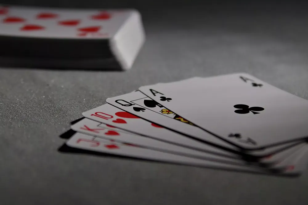 Photo of a stack of playing cards in the background on a table. In the foreground is a royal flush.