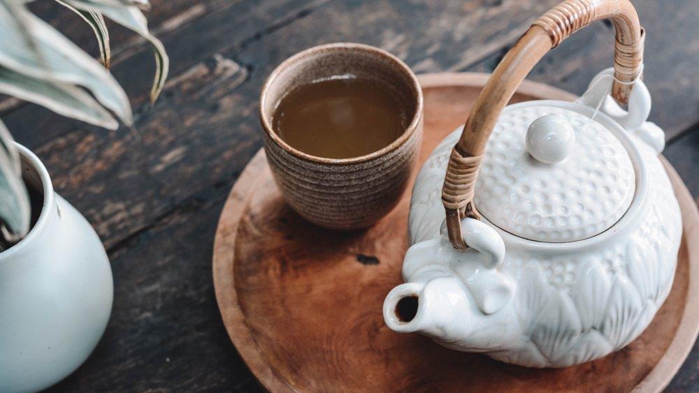 A brown teacup full of tea sitting on a tray next to a white teapot.
