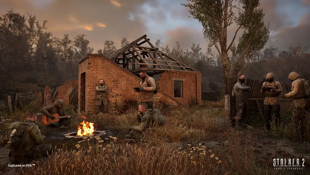 A group of people in warm clothing and gear sitting or standing in small groups around a camp fire.