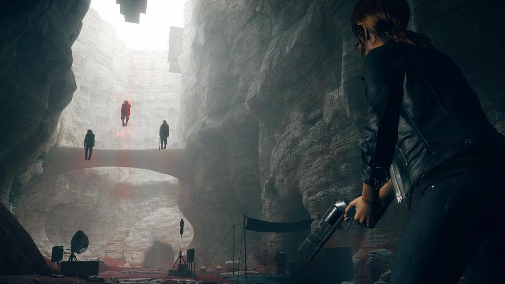 A red-haired woman in a leather jacket and jeans standing in a surreal path lined by tall stone cliffs, several floating humans can be seen ahead of her.