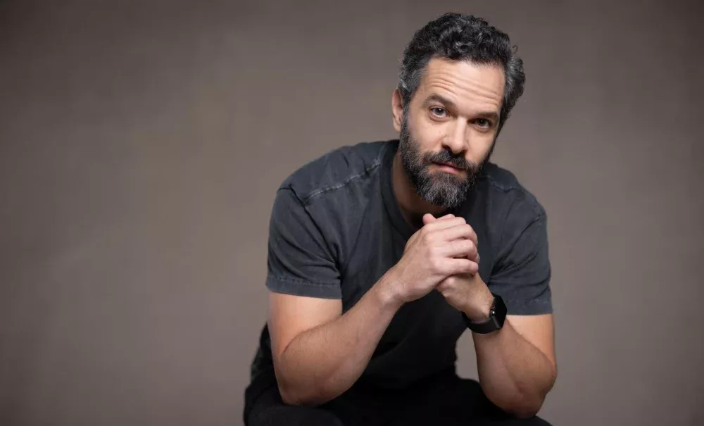 A middle-age man in a dark grey t-shirt and black pants, staring intently at the camera.