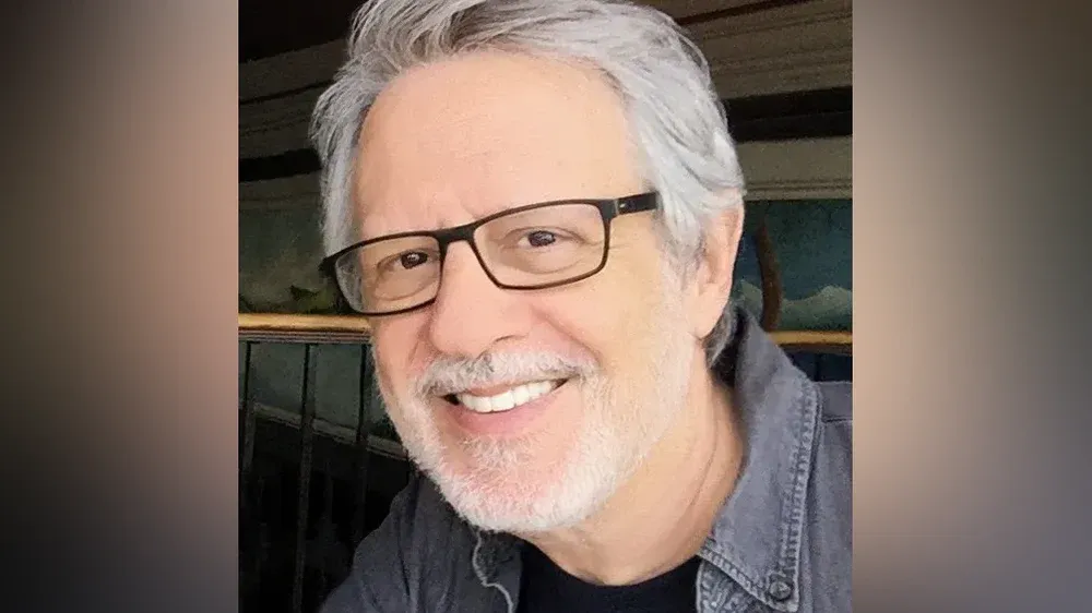 Headshot of a smiling man with grey hair and black rimmed glasses.
