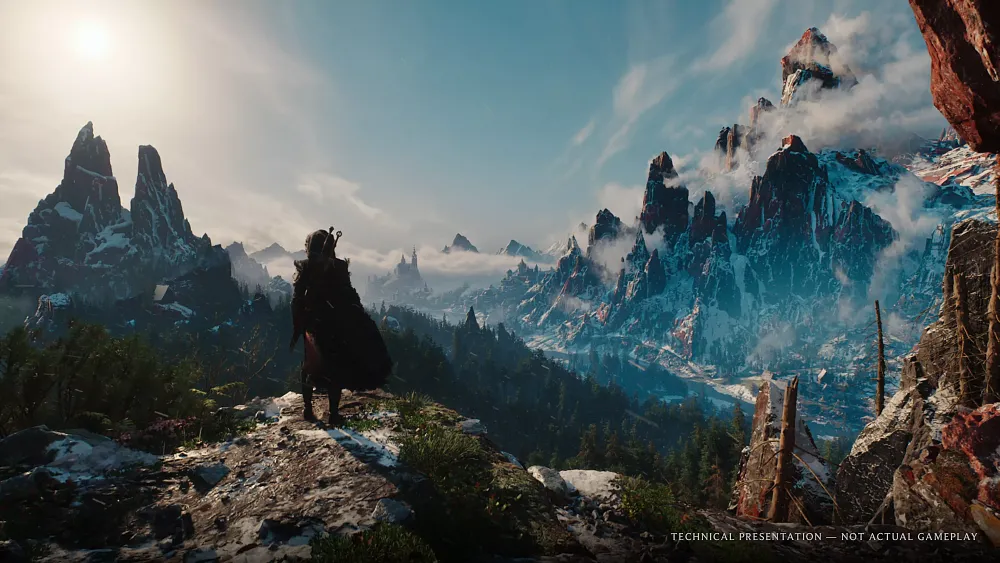 A woman standing on a cliffside viewing distant snow capped mountains.