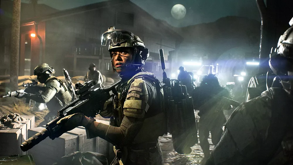 A group of soldiers illuminated by vehicle headlights marches forward at night on the battlefield.