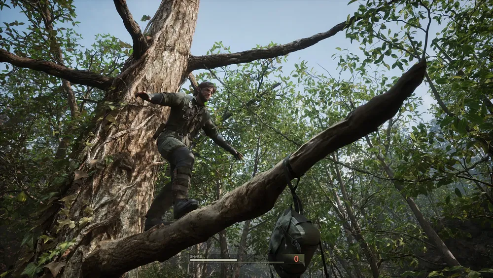 A man in camo balances on a tree limb as he approaches a satchel hanging at the end of the limb.
