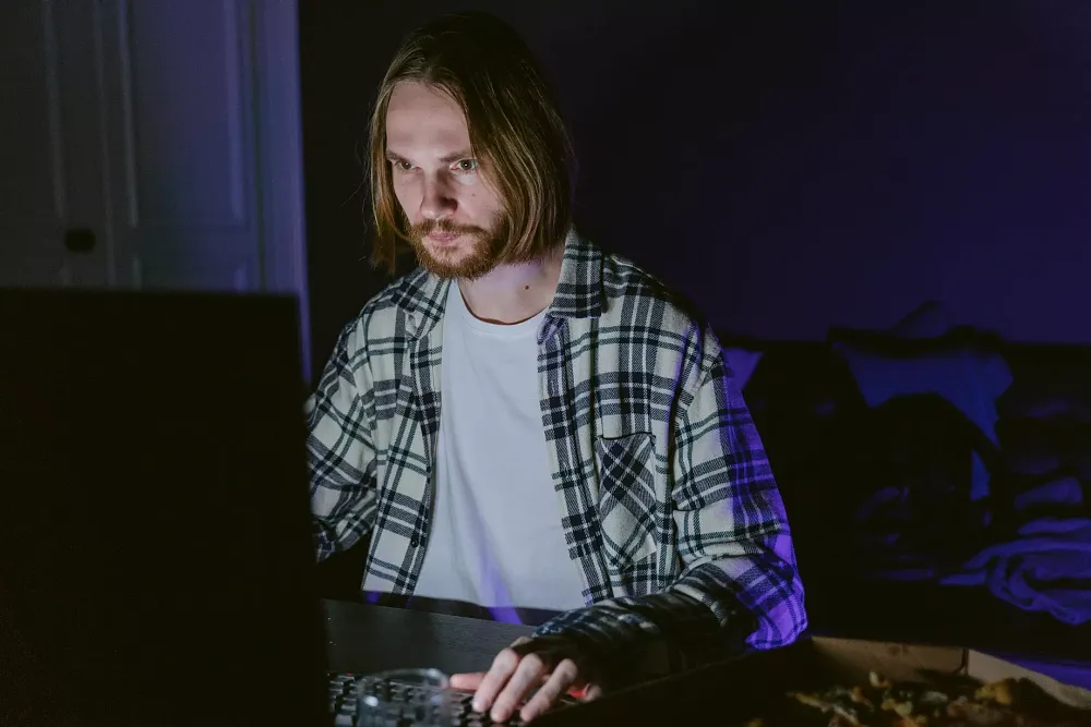 A man using a computer keyboard in a darkened room.