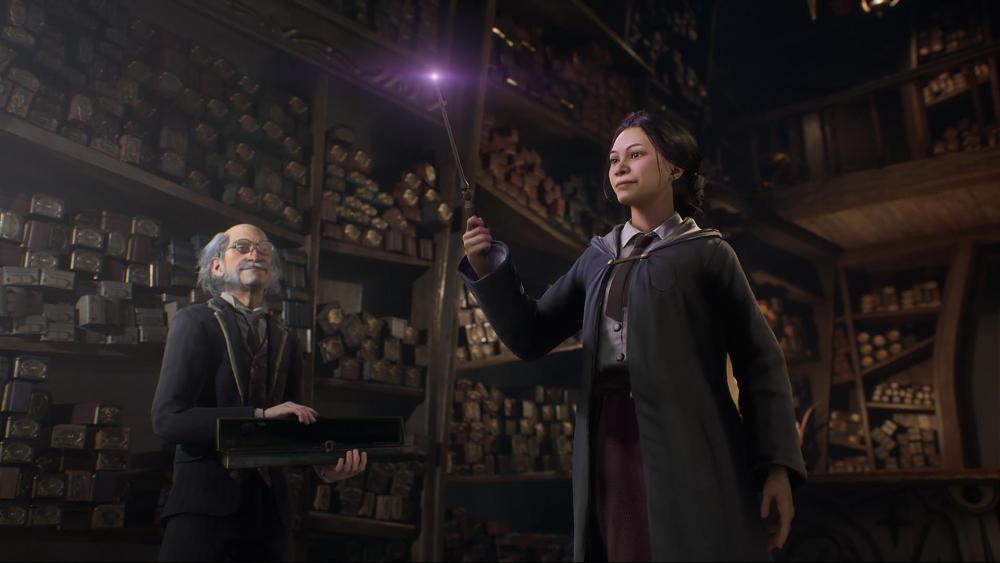 A girl holds a wand while a grey haired, balding man stands nearby. They are standing in front of very tall shelves full of boxes containing other magical wands.