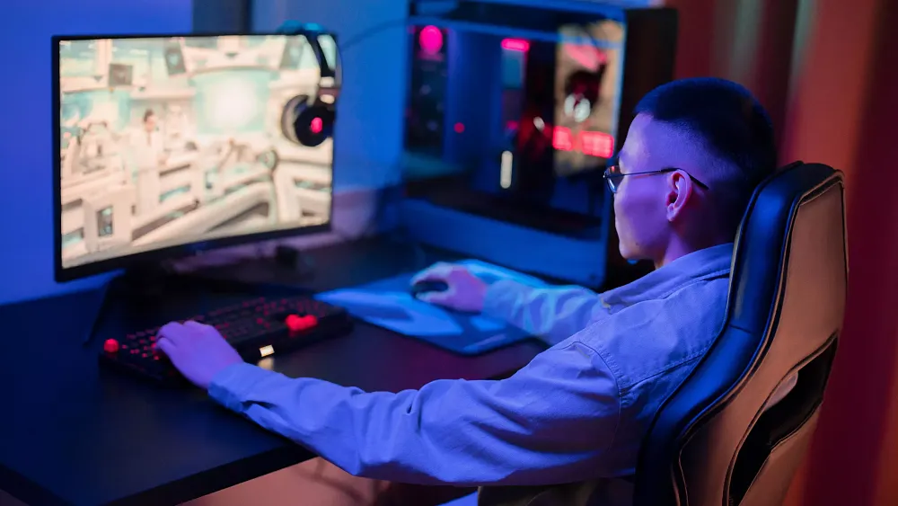 A person sitting at a desk and playing a game on a PC. Source: pexels.com.