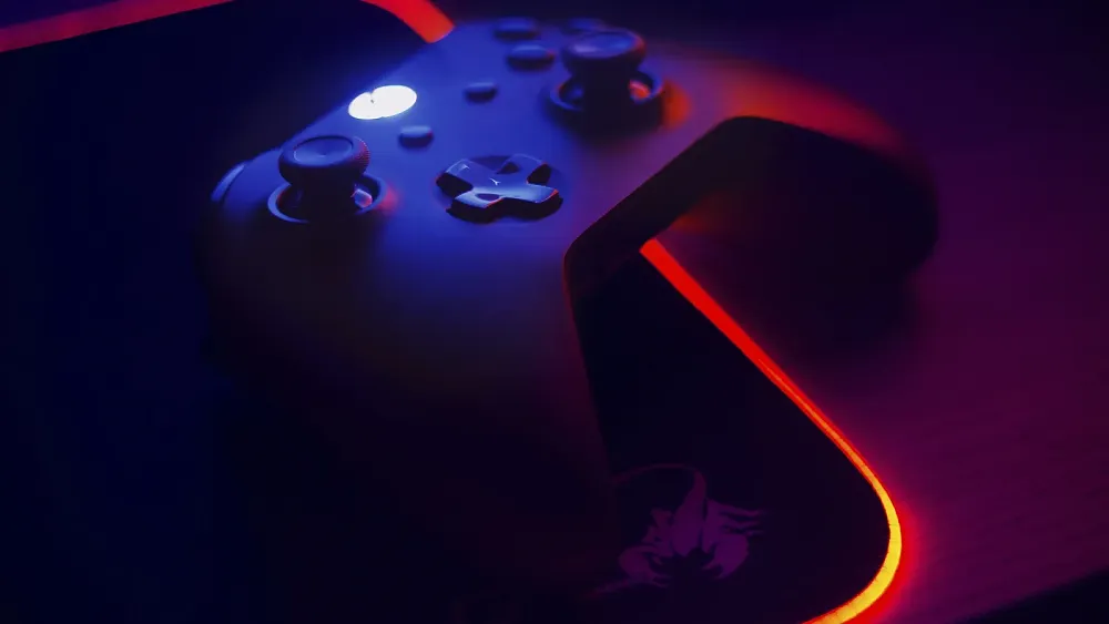 A black Xbox controller on top of a mousepad and both sitting on a desk.