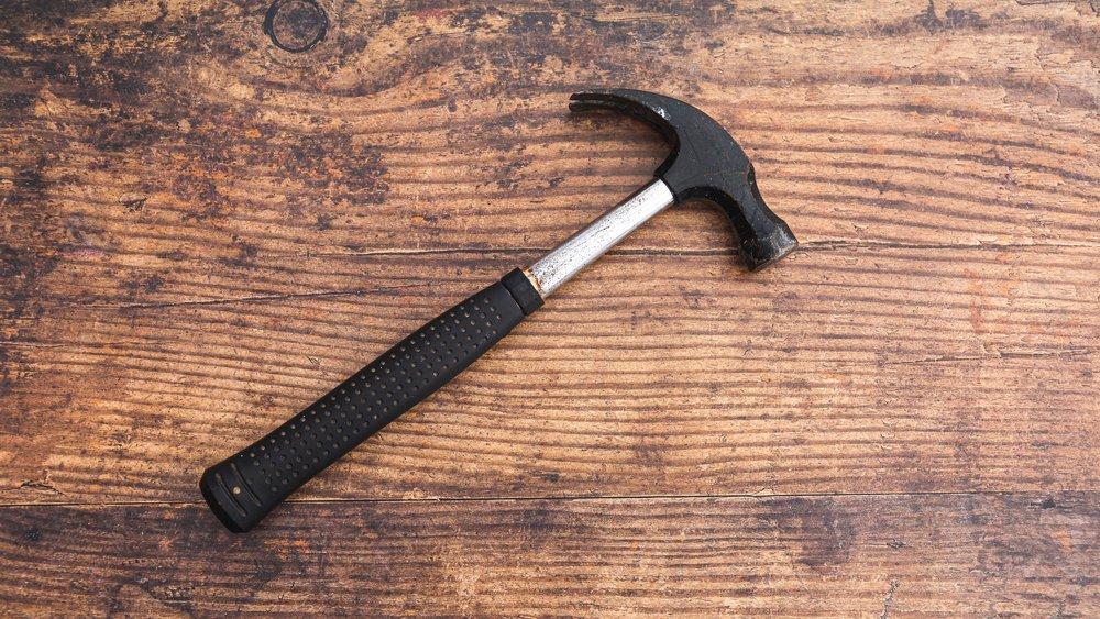 A metal hammer with a rubber grip laying on a wooden table.