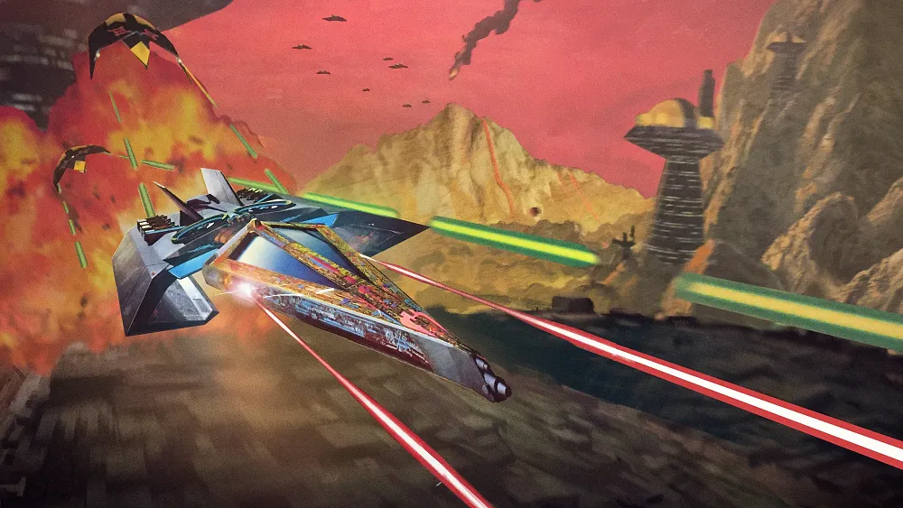 Artwork showing a sci-fi spaceship flying left to right at high speeds. It is firing off lasers while being pursued by other sci-fi style spaceships. Behind the ships a large fireball explosion can be seen.