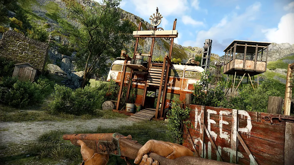 First-person view of a character holding a gun approaching a makeshift settlement with rundown buildings and a lookout tower.