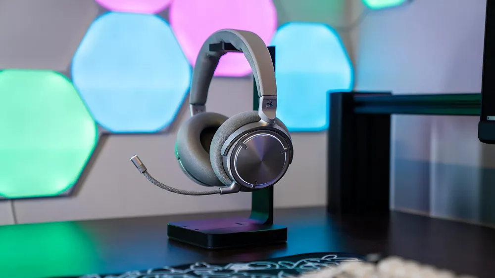 A silver colored gaming headset sitting on a headphone holder on a table.
