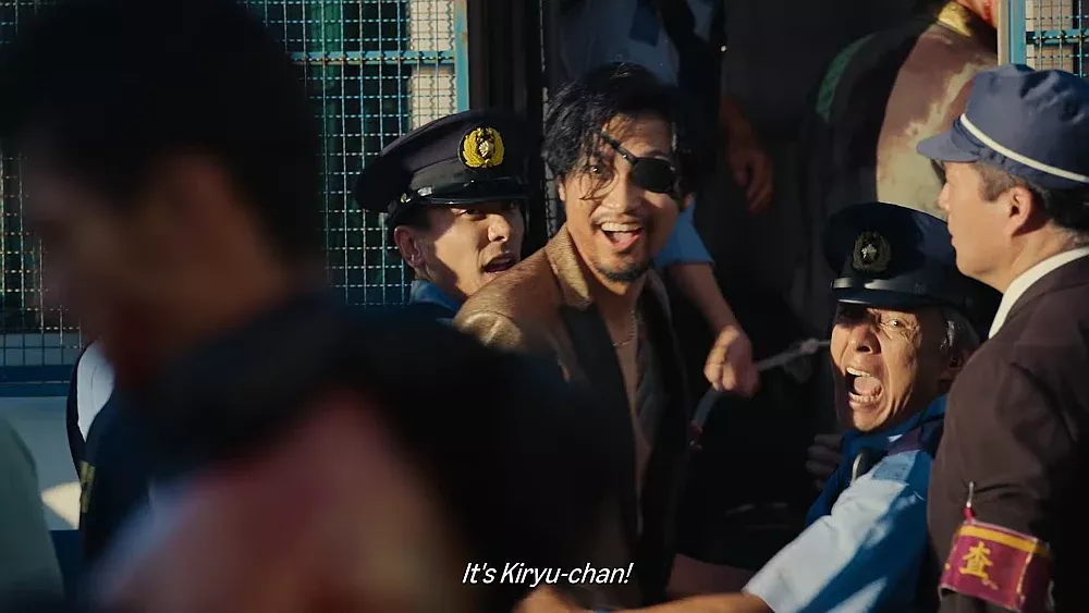 A man with an eye patch is being arrested by the cops while yelling out, "It's Kiryu-chan!"