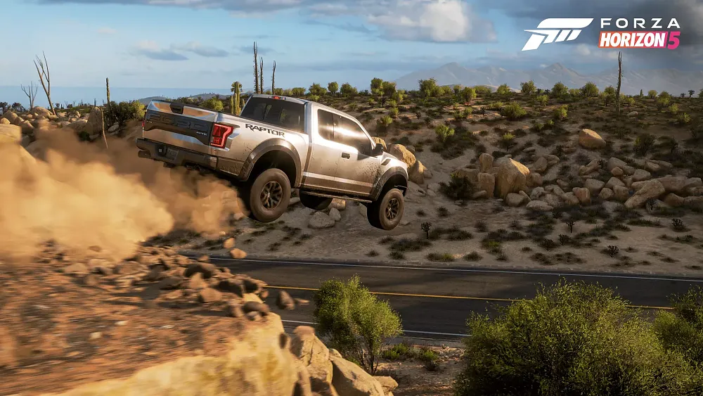 A pickup truck jumping a small ridge in a dusty desert and rocky environment.
