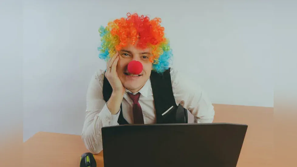 Photo of a clown at a laptop smiling at the camera.
