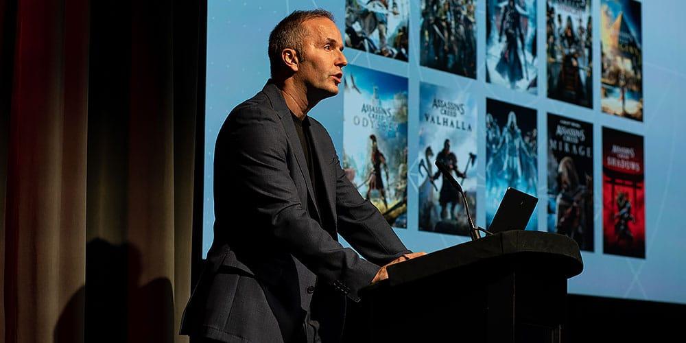Game designer, producer, and developer Marc-Alexis Côté standing at a podium delivering a speech or presentation to an unseen audience.