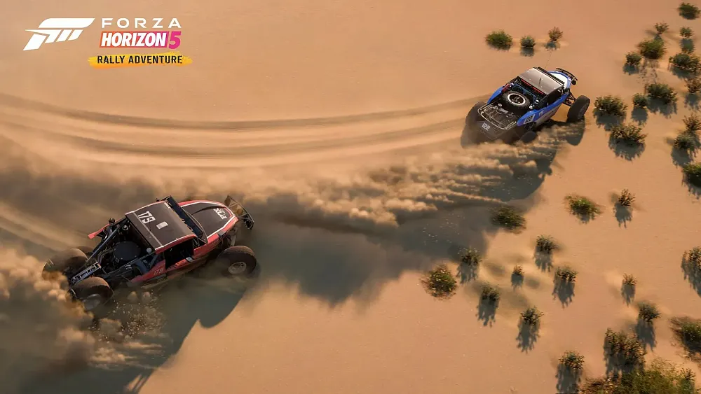 Overhead shot of two rally cars racing through sand dunes.