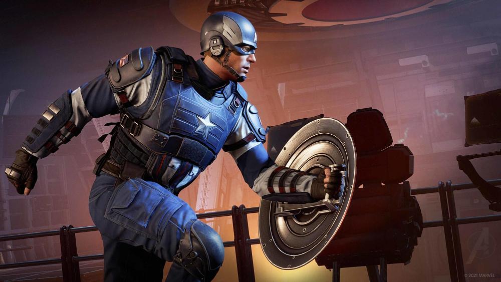 Screenshot of Captain America running to the right. He is dressed in a blue hero suit with some red and white stripes. He is holding a round shield in his left hand. He is running inside a room with metal wall components, a chair, and metal railings.