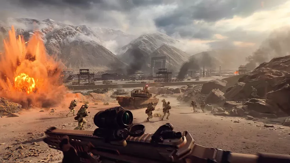 First-person view of a soldier in a modern warfare setting. Other troops and a tank are heading towards an industrial complex. An explosion is going off on the left side of the image.