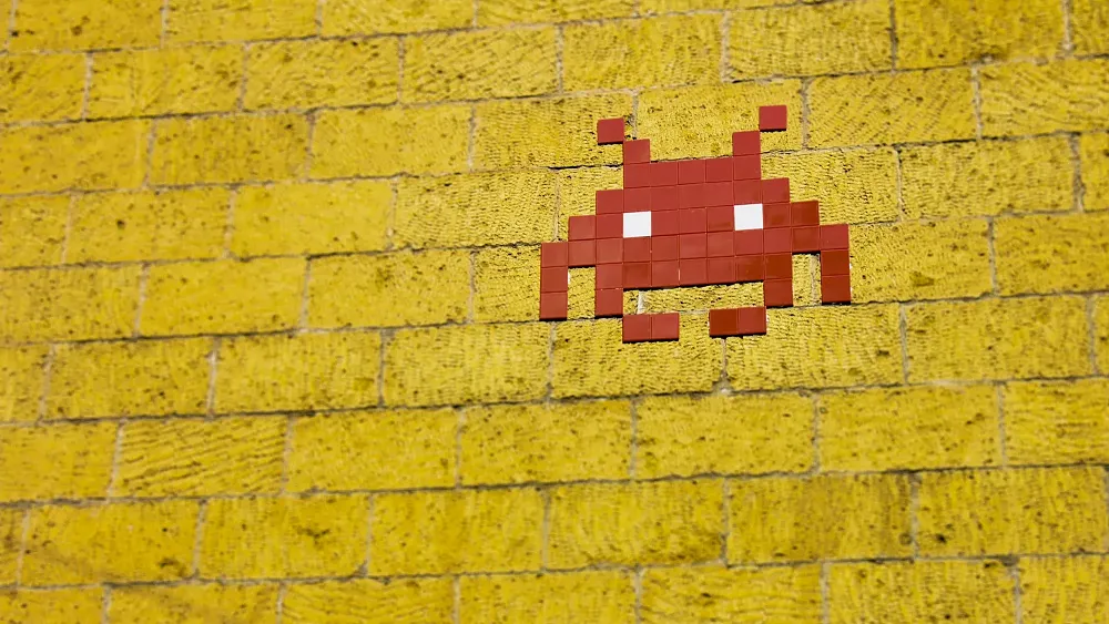 A red invader from Space Invaders on a yellow brick wall.