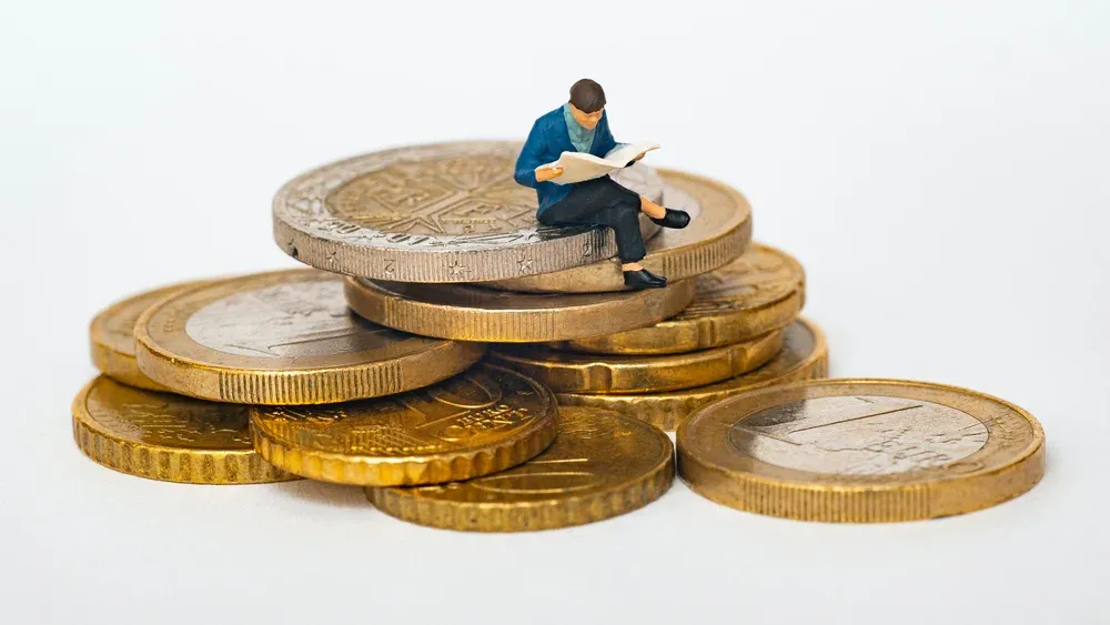 Tiny figure of a man sitting atop a small pile of golden coins.