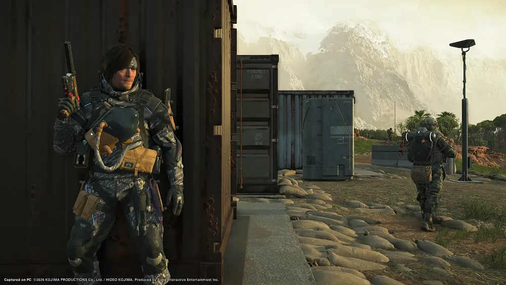 A man with a silenced pistol, wearing a bandana, taking cover behind a crate as an enemy patrol walks away.