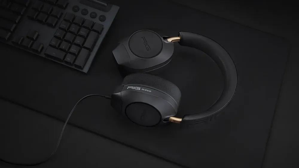 The RIG R5 Spear MAX HD headset laying on a black deskmat next to a black keyboard, all of which is o n a black desk.