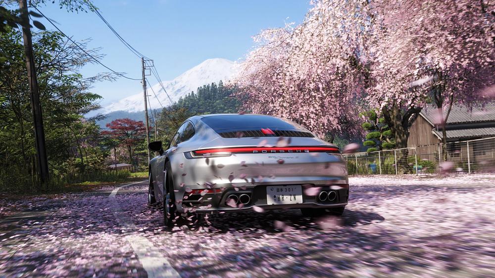 A Porsche racing through the Japan countryside on a road covered with cherry blossom petals.