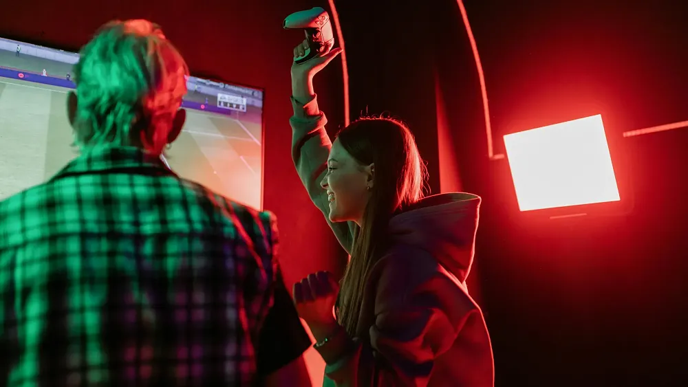 A woman celebrating while playing a video game. Image by a darmel on Pexels.