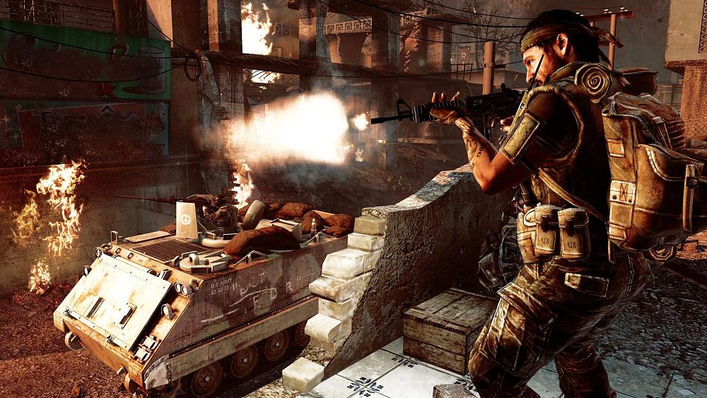 Screenshot showing a soldier wearing a bandana firing an automatic rifle off screen while an armored vehicle rides through ruined city streets nearby.