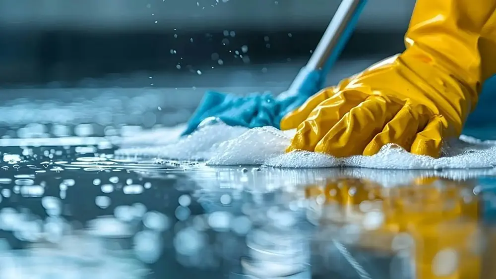 A person with yellow gloves scrubbing a floor with soap and water. Image by PuroClean of Fort Worth on Unsplash.