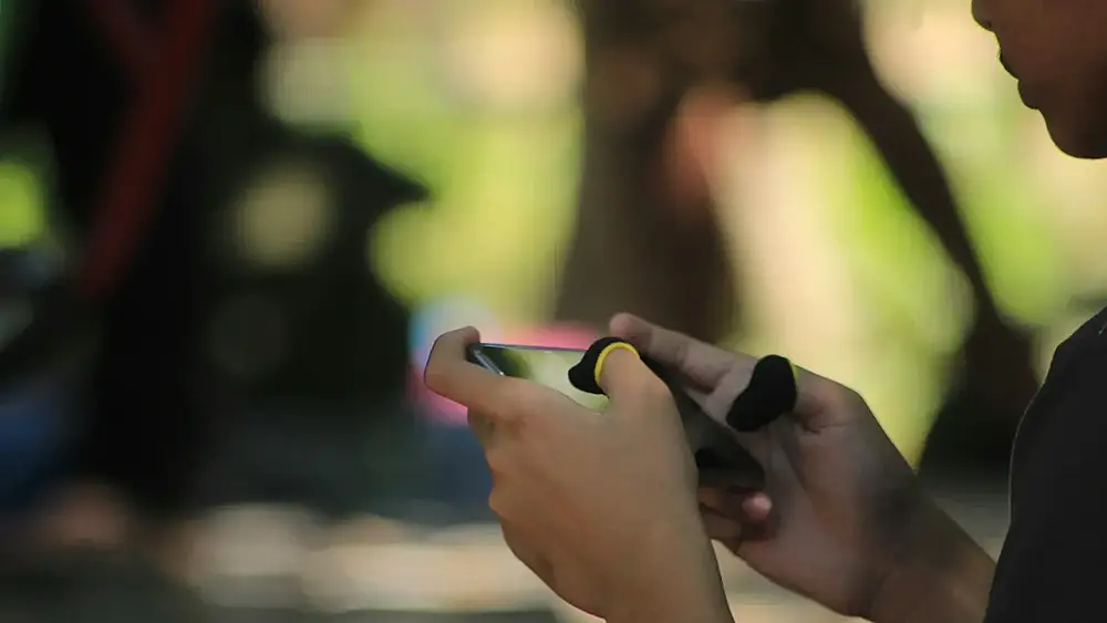 A person playing a mobile game in the park. Image via unsplash.