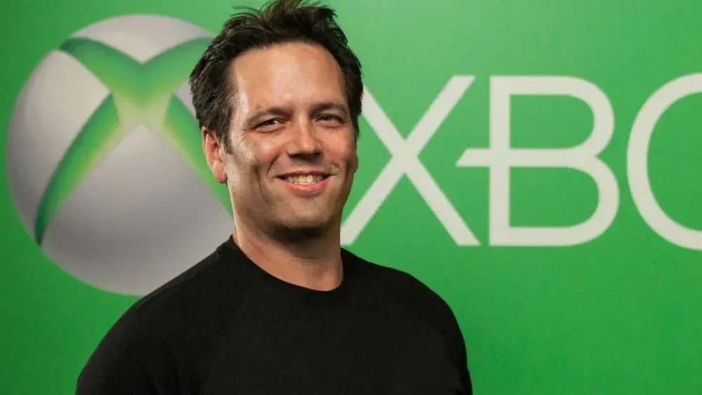 Photograph of a man, Phil Spencer, standing in front of the Xbox logo
