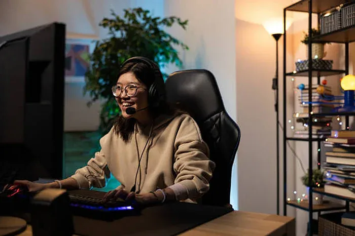 An Asian woman smiling while sitting at a computer possibly playing games