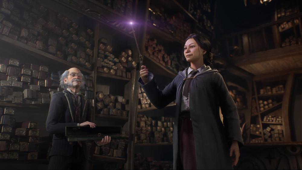 A girl holds a wand while a grey haired, balding man stands nearby. They are standing in front of very tall shelves full of boxes containing other magical wands.