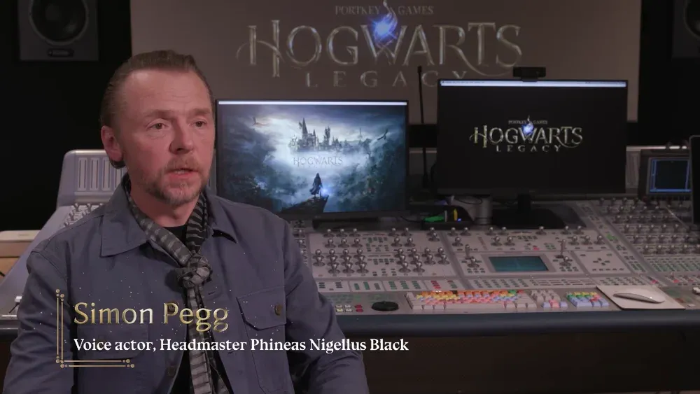 Actor Simon Pegg talking about his role as Headmaster Black in Hogwarts Legacy. He is speaking in front of an audio mixing station that has several dozen dials and sliders. Logos for Hogwarts Legacy adorn several monitors behind Simon Pegg.